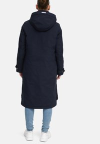 Langer, dunkelblauer Mantel mit Kapuze, ausgestattet mit einer glatten Textur und knöpfbaren Manschetten, getragen über hellblauen Jeans und weißen Turnschuhen.