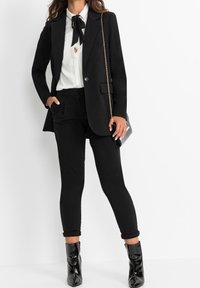 Czarna, dopasowana marynarka na białej koszuli z czarną muszką, w połączeniu z czarnymi, obcisłymi spodniami i błyszczącymi czarnymi botkami.