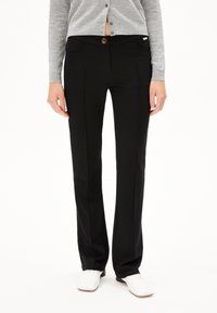 Zwarte op maat gemaakte broek met een gladde textuur, voorzien van een knoopsluiting, zijzakken en subtiele plooidetails langs de benen.