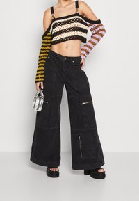 Pantaloni cargo neri a gamba larga con tasche a toppa e zip, abbinati a un top a maglia corto multicolore con maniche lunghe a righe.