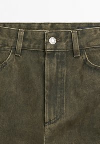 Jeansy w oliwkowym kolorze o wysokim stanie, z zapięciem na guziki z przodu, szlufkami na pasek i widocznymi przednimi kieszeniami.