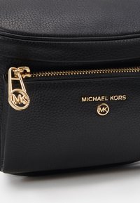 Black leather handbag with a textured surface. Features a gold zipper, gold branding, and a round logo accent near the zipper.