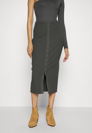 Slim-fit, geribbelde midi-rok in donkergrijs met knopen aan de voorkant, gecombineerd met beige suède enkellaarsjes op een model.