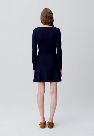 Abito a maglia lungo navy con corpino aderente e gonna svasata. Tessuto liscio, scollo rotondo, dettagli minimi, abbinato a scarpe marroni.