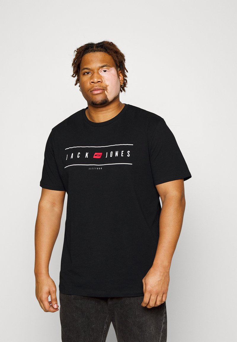 Must värvi puuvillane T-särk, mille esiküljel on valge ja punane "JACK & JONES" graafika, lühikesed varrukad ja ümar kaelus.