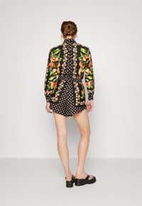 Blusa de estampado floral con pantalones cortos de lunares, fondo negro, mangas largas, cintura ceñida y un cuello. Combinada con sandalias negras gruesas.