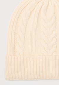 Cream-colored knitted beanie with cable knit and ribbed fold-over cuff detailing on a light background.