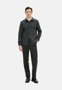 Gray wool jacket with two chest pockets, button closure, and a polished collar; paired with dark gray trousers and black shoes.