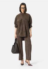 Camisa de ante marrón con botones y dos bolsillos en el pecho, combinada con pantalones de ante a juego. Un bolso negro y tacones de estampado de leopardo completan el conjunto.