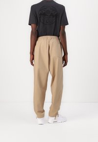 Černé tričko s krátkým rukávem s kruhovým potiskem na zádech, doplněné volnými béžovými kalhotami a bílými teniskami.