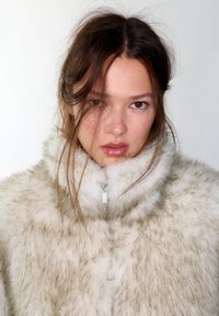 Giacca in ecopelliccia in tonalità crema e marrone chiaro, con colletto alto e chiusura con zip. Texture morbida con aspetto soffice.