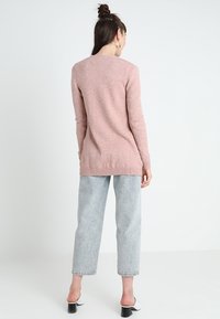 Ljusrosa stickad tröja med långa ärmar, ribbat fåll och en avslappnad passform, i kombination med ljusblå högmidjade jeans och svarta klackskor.