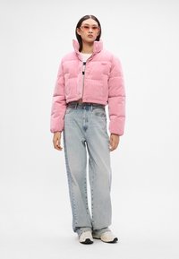 Rózsaszín corduroy r�övidített puffermellény magas gallérral, gombos záródással és két elülső zsebből áll, világoskék egyenes szárú farmernadrággal párosítva.
