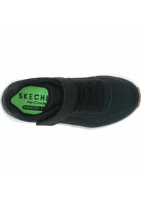Zapatilla deportiva negra con parte superior de malla, banda elástica, cierre de cordones, plantilla verde y suela de goma blanca con acentos marrones.