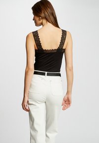 Top nero senza maniche con spalline in pizzo a scallop, abbinato a jeans bianchi a vita alta. Il tessuto è morbido e presenta un design aderente.