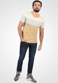 Beige og grå kortærmet T-shirt med rund halsudskæring, parret med mørkeblå jeans og grå sneakers med hvide striber.