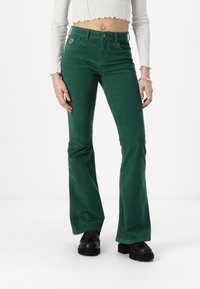 Green corduroy flared pants with a fitted waist, front pockets, and a metallic button. The fabric has a soft, textured finish.