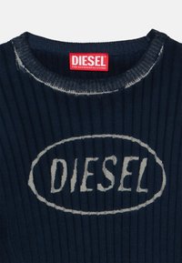 Μπλε ναυτικό ριμπ πουλόβερ με στρογγυλή λαιμόκοψη, με το λευκό οβάλ "DIESEL" στο μπροστινό μέρος και μια κόκκινη ετικέτα στο εσωτερικό του γιακά.