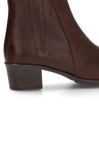 Botín de cuero marrón hasta el tobillo con un tacón bajo y cuadrado, que presenta paneles laterales elásticos y una textura suave. Detalle de costura sutil a lo largo de las costuras.