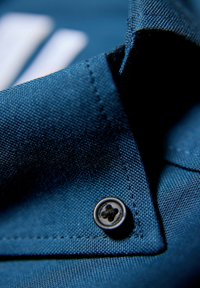 Blauwe stoffen kraag met een gestructureerde weving, voorzien van een zwarte knop met een ronde vorm en stiksels langs de rand.