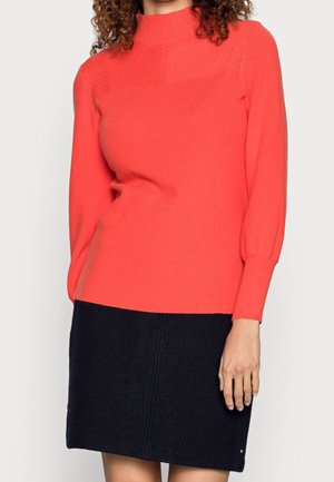 Sweter dzianinowy w jasnym koralowym kolorze z wysokim kołnierzem i prążkowaną teksturą, połączony z ciemnonawym spódnicą z detalem szwu.