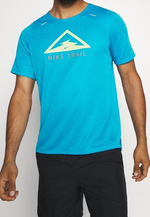 Man draagt een felblauw Nike Trail T-shirt met korte mouwen en zwarte korte broek, staand tegen een effen witte achtergrond.