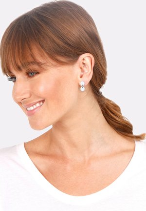 Boucles d'oreilles en argent en forme d'éclats circulaires, l'un plus grand au sommet, reliés par une fine tige, sur un fond clair.