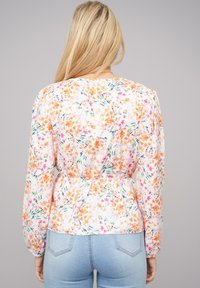 Blusa floreale bianca con motivi arancioni, rosa e verdi. Maniche lunghe, scollo rotondo e dettaglio arricciato sul retro. Texture del tessuto morbida.