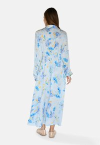 Rochie maxi florală din material albastru deschis cu modele florale albastre și galbene, cu mâneci lungi și talie strânsă, având o fustă fluidă.
