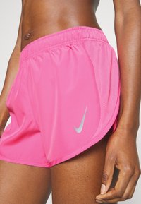 Pantalones cortos deportivos rosas hechos de tela ligera, con un panel de malla y un logo plateado de Nike en el lateral, con una cintura elástica.
