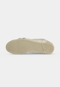 Semelle d'une chaussure Reebok beige clair avec un motif de crampons en nid d'abeille et le logo Reebok près du talon.