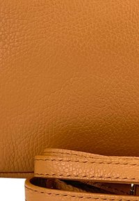 Tan leren schoudertas met een gestructureerd oppervlak, voorzien van een platte schouderriem en zichtbare stiksels langs de randen.