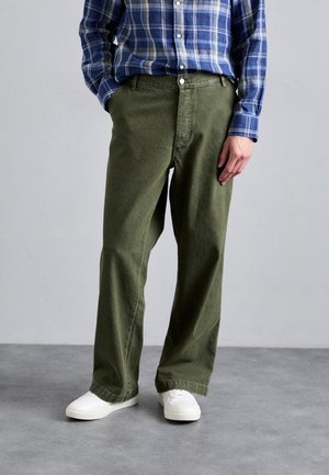 Pantalons évasés vert olive en tissu résistant, accompagnés d'une chemise à carreaux bleus à boutons et de baskets blanches. Avec poches avant.