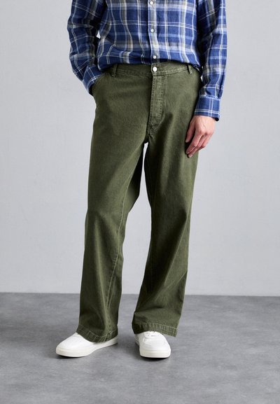 Olijfgroene wijde broek van stevig materiaal, gecombineerd met een blauw geruite overhemd met knopen en witte sneakers. Bevat voorzakken.
