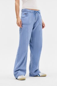 Calças largas riscas azul claro com cintura elástica, apresentando bolsos frontais e uma textura suave. As riscas correm verticalmente ao longo do tecido.