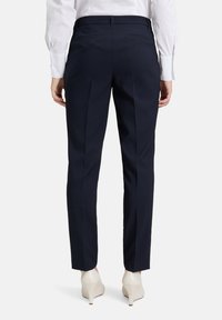 Marina skräddarsydda byxor med en slät yta, utrustade med två bakfickor och en smal passform, matchade med vita högklackade skor.