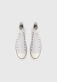 Hvite høyhælte sneakers med en glatt lerretsoverdel, rund tåhette, gummisåle og kontrasterende svart stripe rundt sålen.