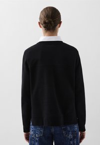 Sudadera negra con cuello blanco, mangas largas y corte relajado. Textura suave y detalle de costura en la parte superior de la espalda.