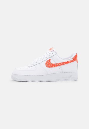 Biały niskoprofilowy sneaker z perforowanym czubkiem, pomarańczowym wzorem paisley na logo Nike i uchwytem na pięcie oraz białą gumową podeszwą.