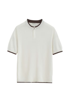 Chemise en maille blanche à manches courtes avec un liseré brun foncé au col, aux poignets et à l'ourlet, présentant une courte patte de boutonnage au niveau de l'encolure.