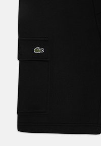 Pantaloni cargo neri in cotone, con una tasca cucita e un piccolo logo di coccodrillo ricamato in verde sul lato.