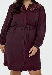 Vinfärgad skjortklänning med spetsdetaljer på axlarna, långa ärmar, knapplåsning framtill och ett knytbälte i midjan. Slät textur.