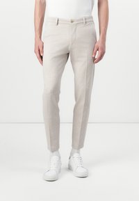 Pantalons ajustés beige clair en tissu doux, dotés de poches avant, d'une coupe slim et d'un ourlet à revers. Assortis avec des baskets blanches.