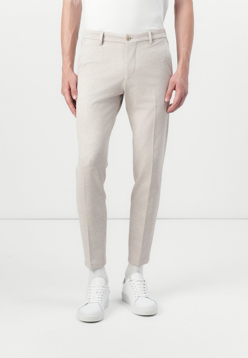 Pantalons ajustés beige clair en tissu doux, dotés de poches avant, d'une coupe slim et d'un ourlet à revers. Assortis avec des baskets blanches.