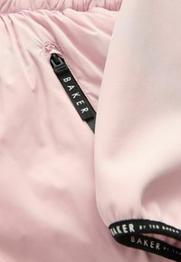 Gaiši rozā jakas audums ar gludu tekstūru, kas aprīkots ar rāvējslēdzēja kabatu un melnu logotipa joslu pie piedurknes ar nosaukumu "BAKER by TED BAKER."