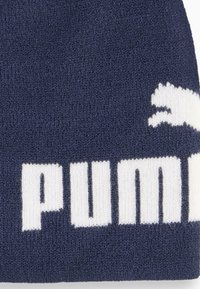 Stickad marinblå mössa med en stor vit Puma-logga och text. Tyget har en mjuk textur och bärs vanligtvis i kallt väder.