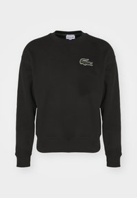 Felpa nera in cotone con scollatura tonda. Presenta un piccolo logo del coccodrillo verde Lacoste sul lato sinistro del petto. Polsini e orlo a costine.