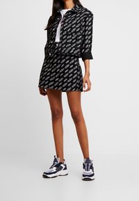 Svart kort jacka och matchande kjol med vitt mönster. I kombination med vita och marinblå sneakers som visar texturerad tyg och kontrasterande accenter.