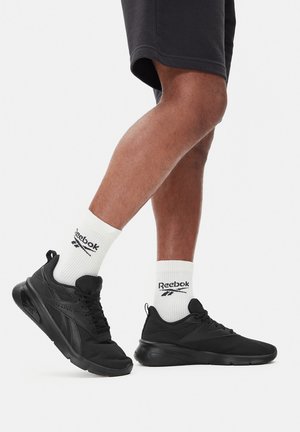 Czarne buty sportowe z teksturowaną siateczkową cholewką i gumową podeszwą. Noszone z białymi skarpetkami Reebok z logo. Szorty widoczne powyżej kolana.