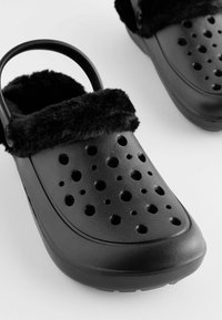 Schwarze Clogs mit weichem schwarzen Futter, ausgestattet mit mehreren Belüftungsöffnungen, einem konturierten Design und einem hinteren Riemen für einen sicheren Sitz.